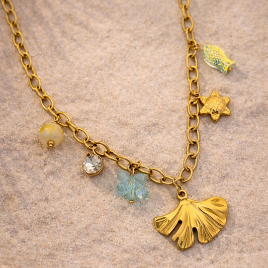Gold necklace with various charms on a sandy background