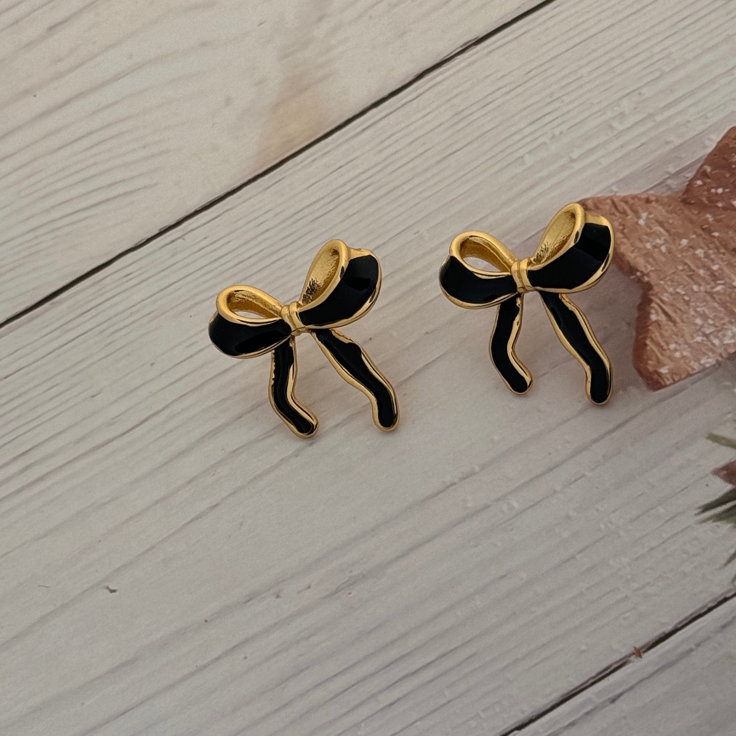 Pair of black and gold bow-shaped earrings on a light wooden surface