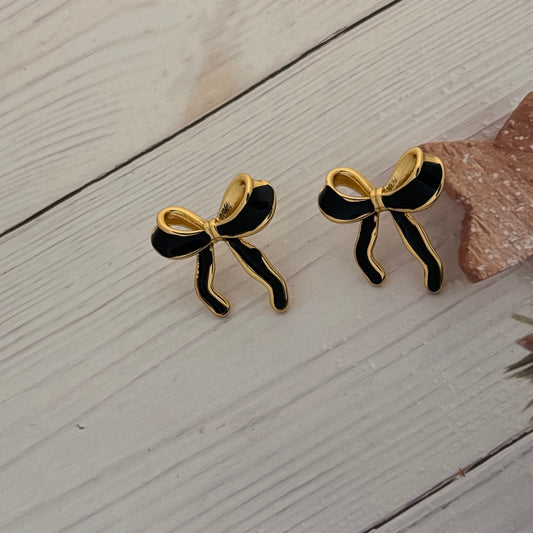 Pair of black and gold bow-shaped earrings on a light wooden surface