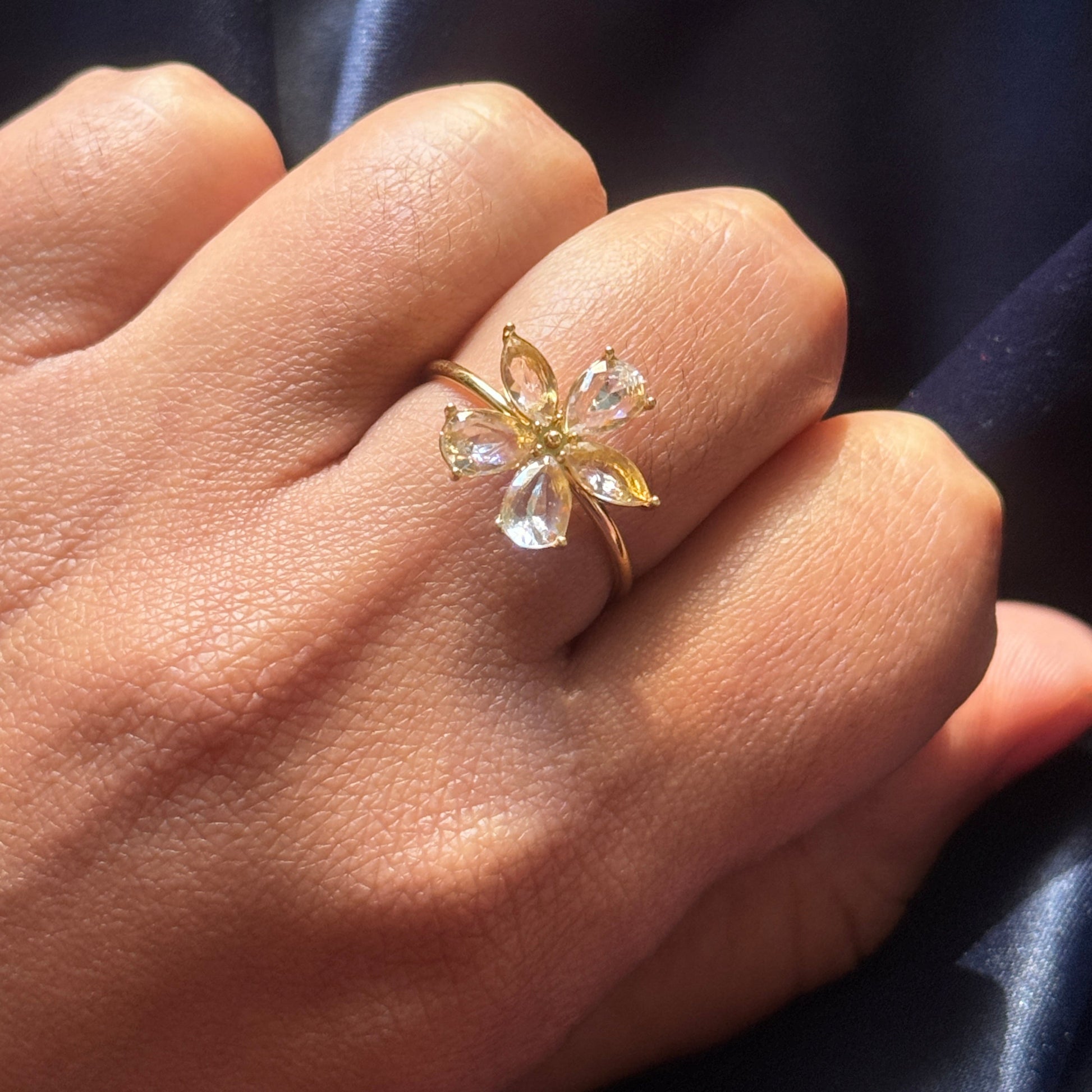Gold ring with clear gemstones on a hand against a dark fabric background