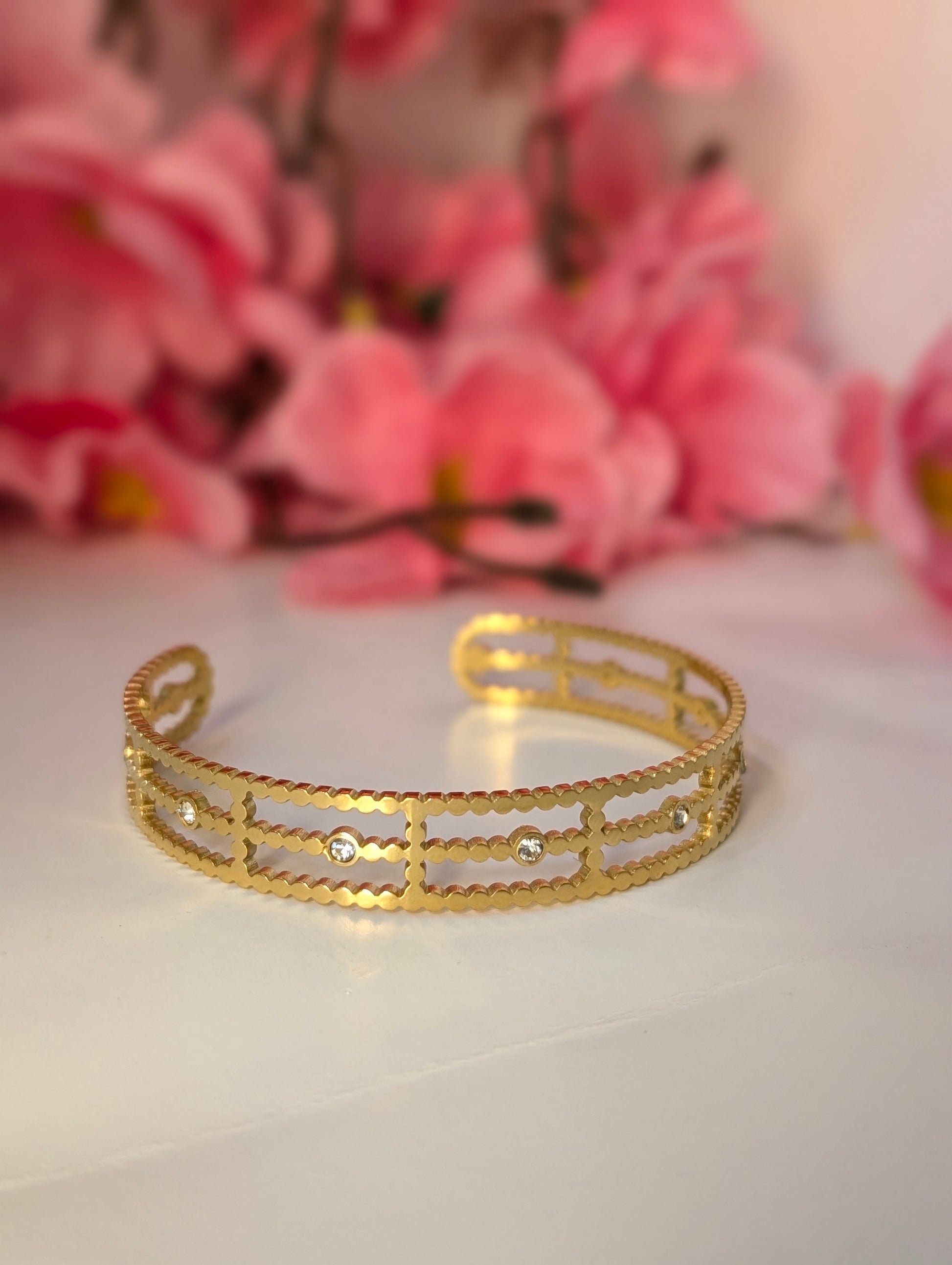Gold bracelet on a white surface with pink flowers in the background
