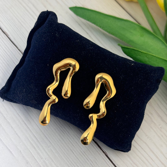 Gold earrings on a navy blue pillow with yellow flowers in the background