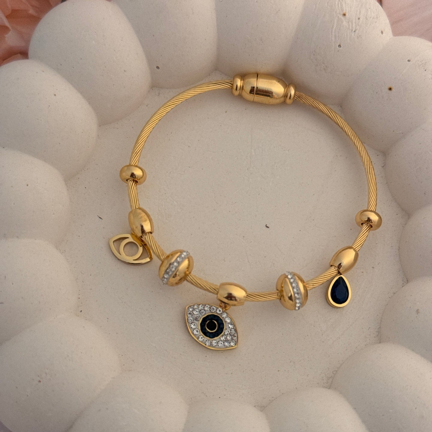 Gold bracelet with an eye-shaped charm on a textured white surface