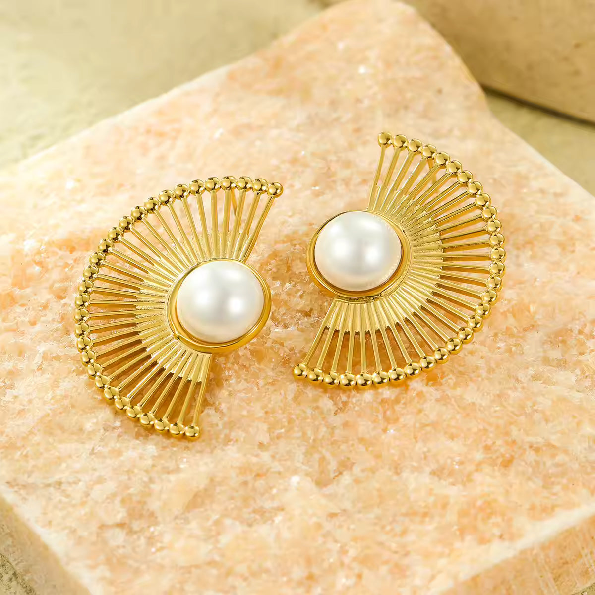 Gold earrings with pearl centers on a textured stone surface