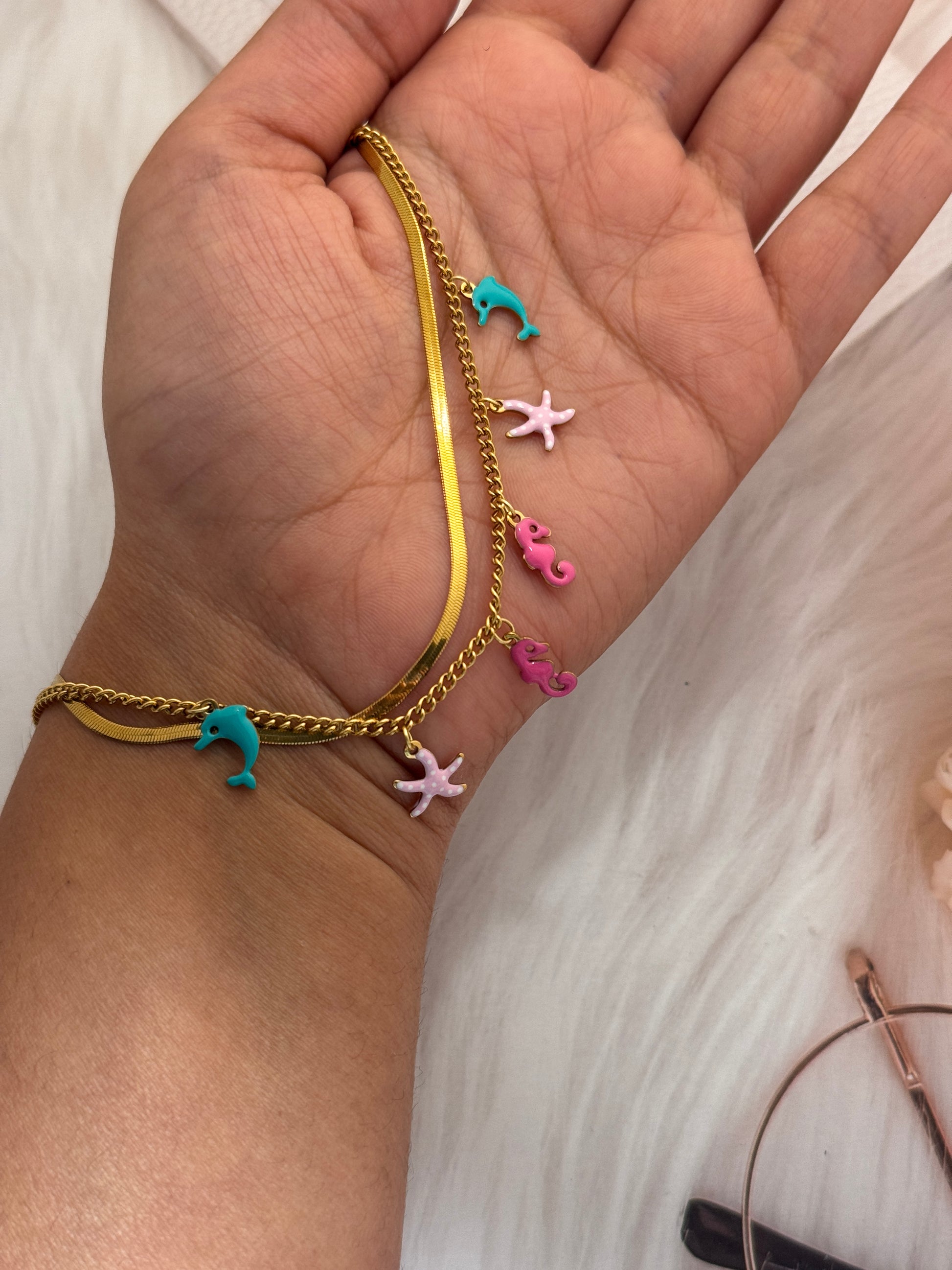 Gold bracelet with colorful charms on a wrist against a white background
