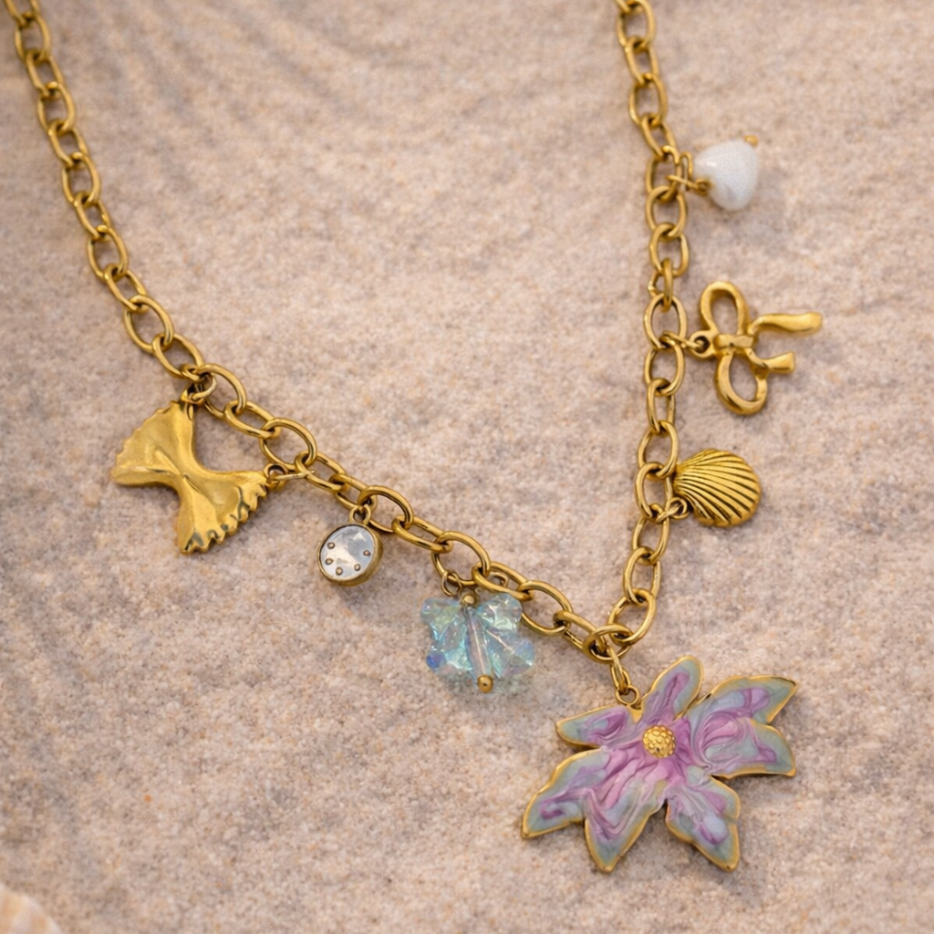 Gold necklace with floral and shell charms on a sandy background