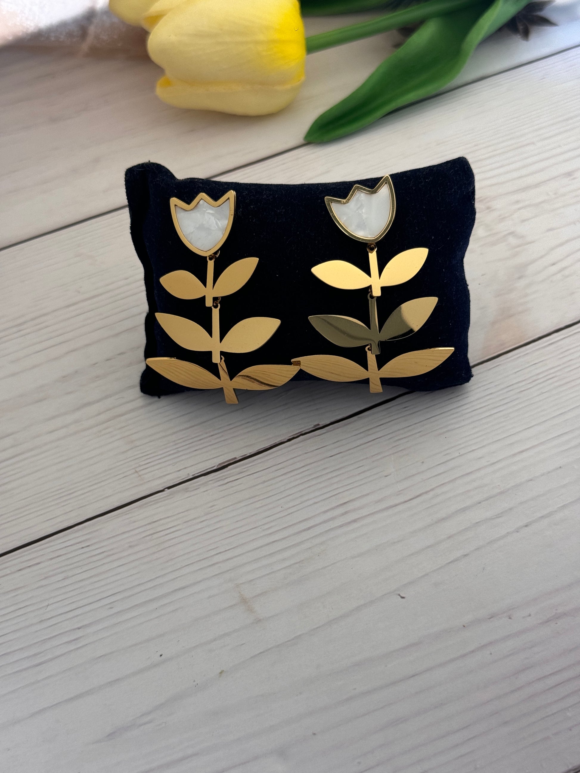 Black pouch with gold leaf design on a light wooden surface next to a yellow tulip.