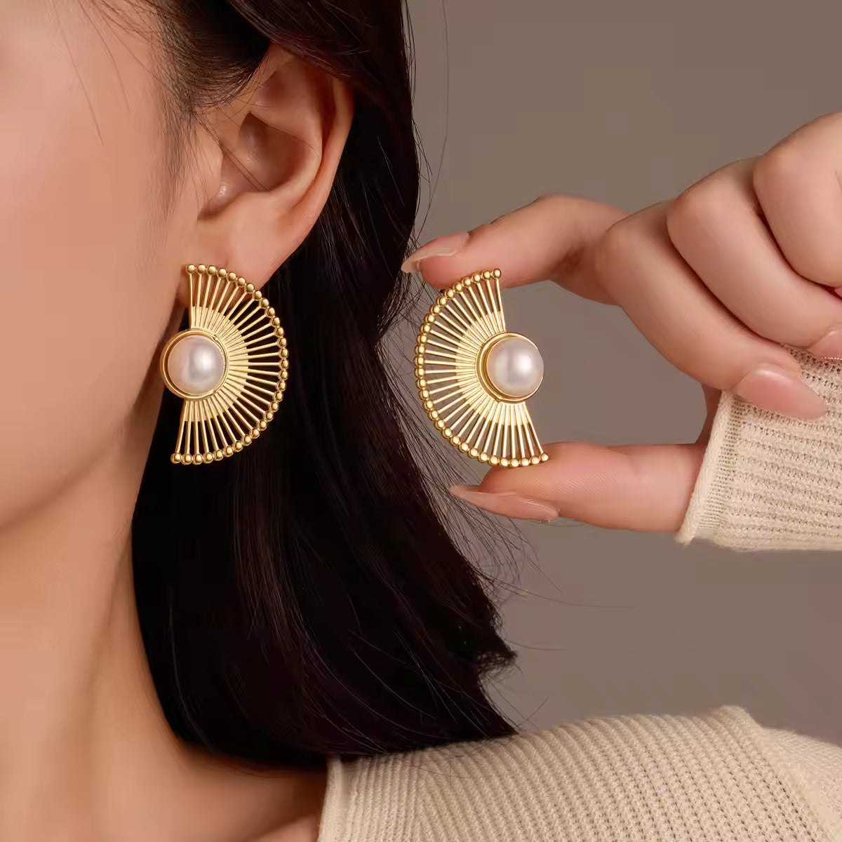 Gold earrings with pearl center worn by a person against a neutral background