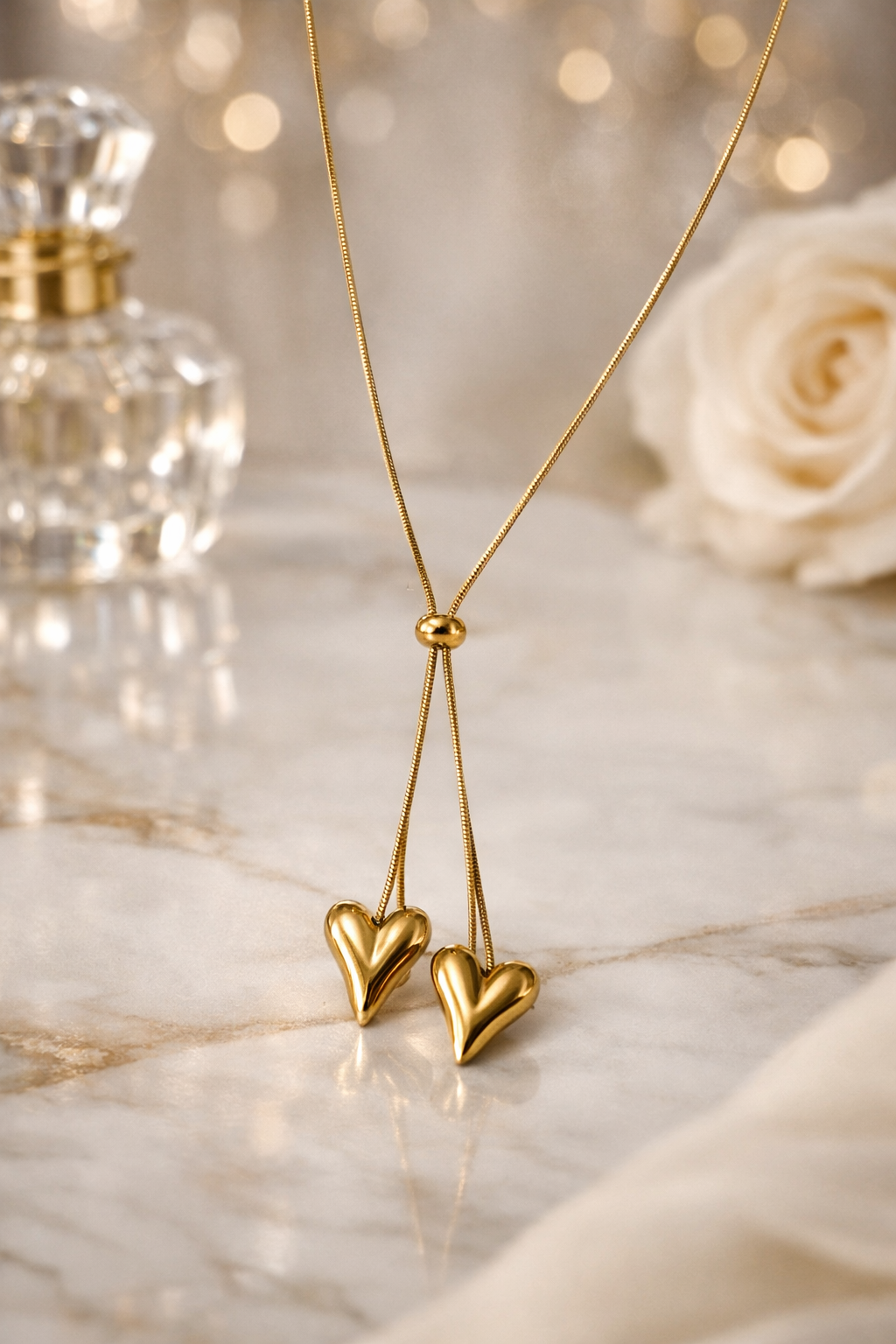 Gold heart-shaped earrings on a marble surface with a rose and perfume bottle in the background.