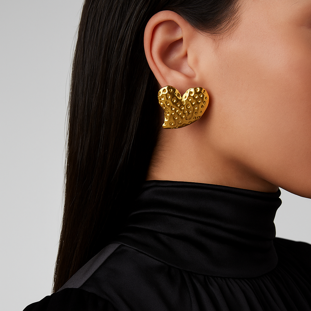 Gold heart-shaped earrings worn by a person with a plain background