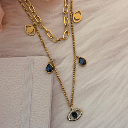 Gold chain necklace with black gemstones on a textured white surface.