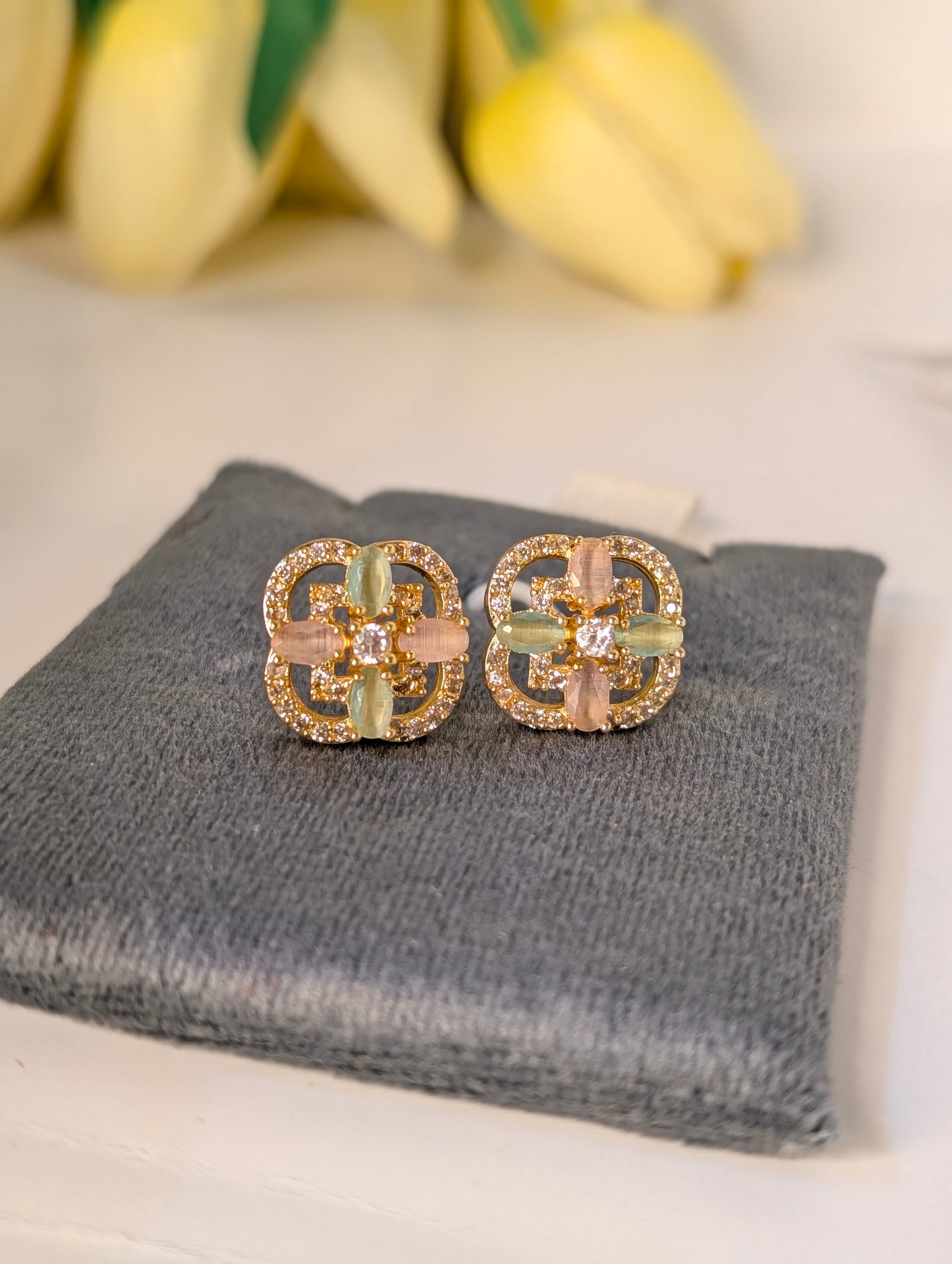 Pair of gold and green earrings on a gray surface with yellow flowers in the background