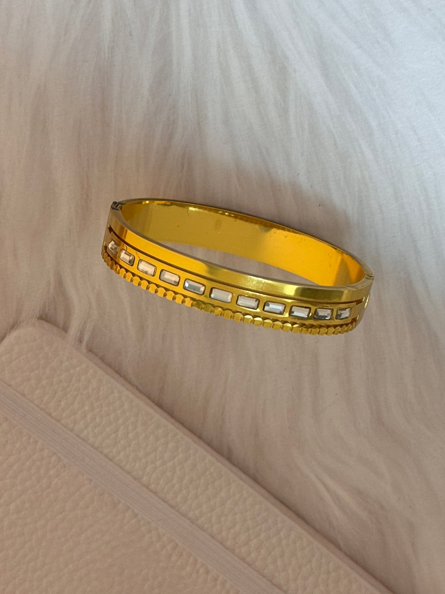 Gold bracelet with embedded stones on a textured beige surface