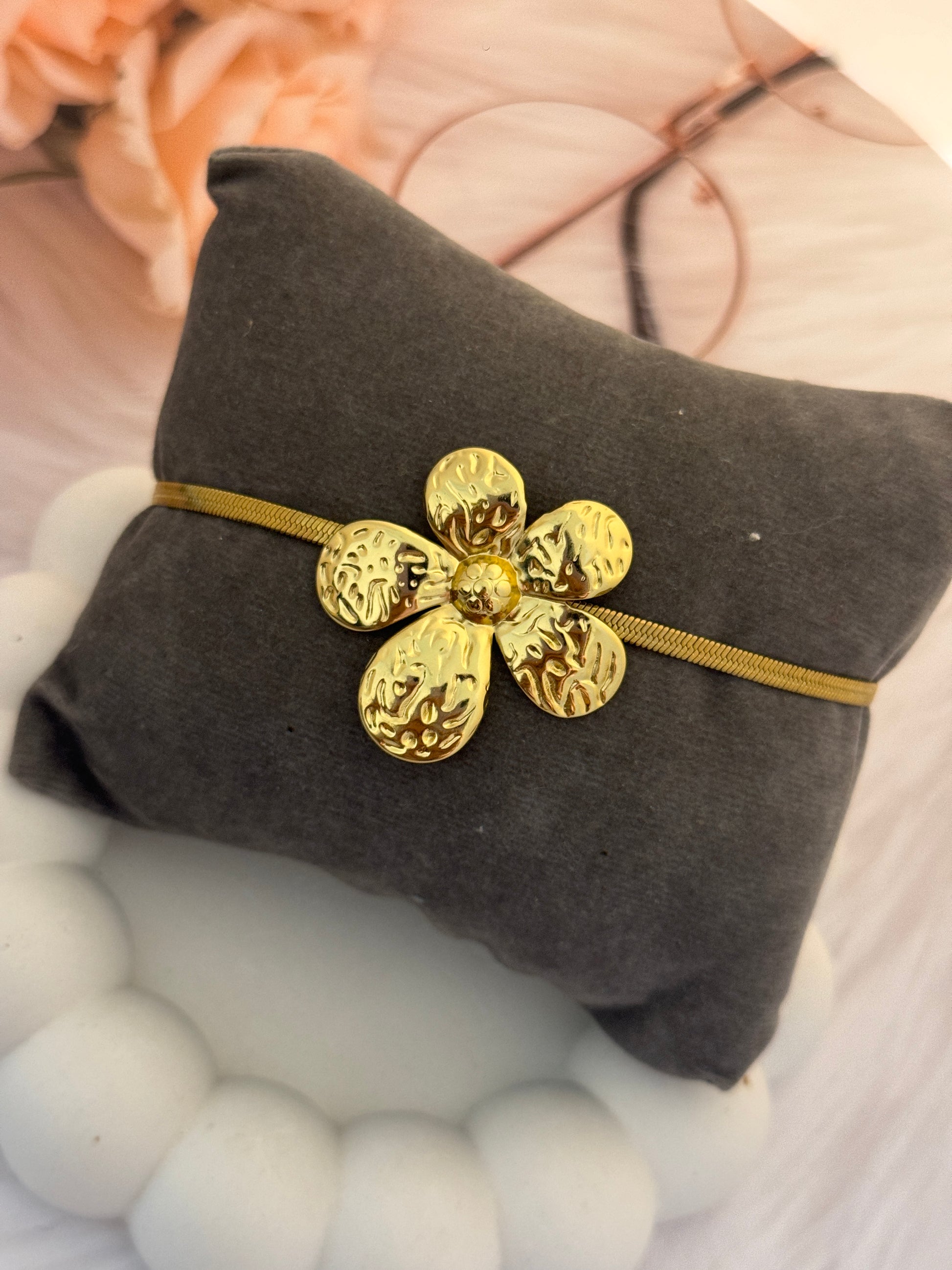Gold flower-shaped pendant on a gray cushion with a blurred floral background
