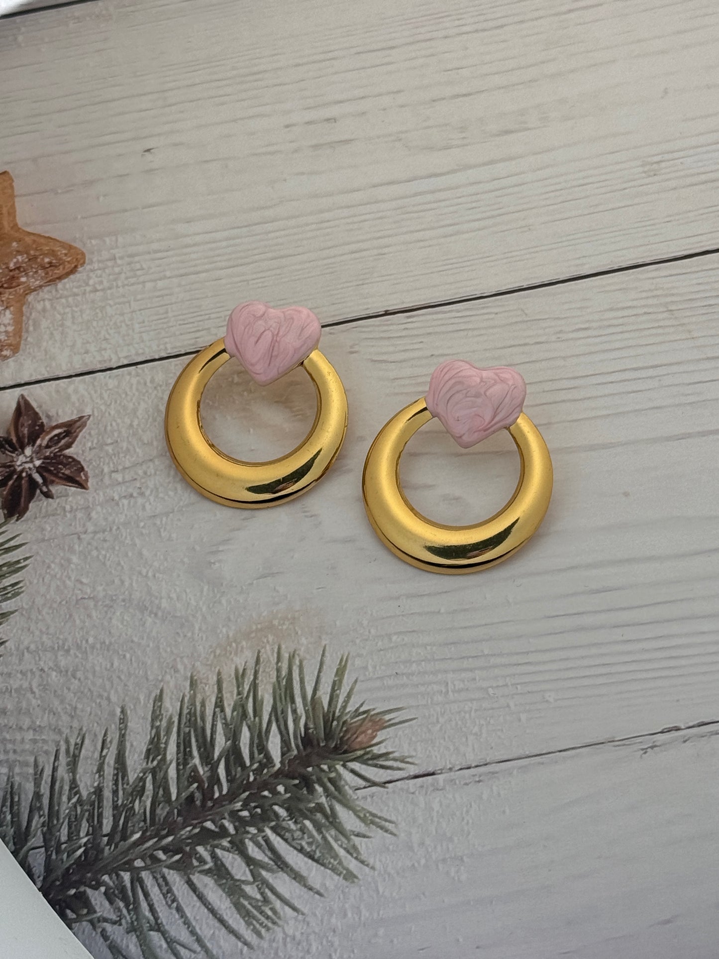 Two gold decorative rings with pink flower-shaped ends on a wooden surface.