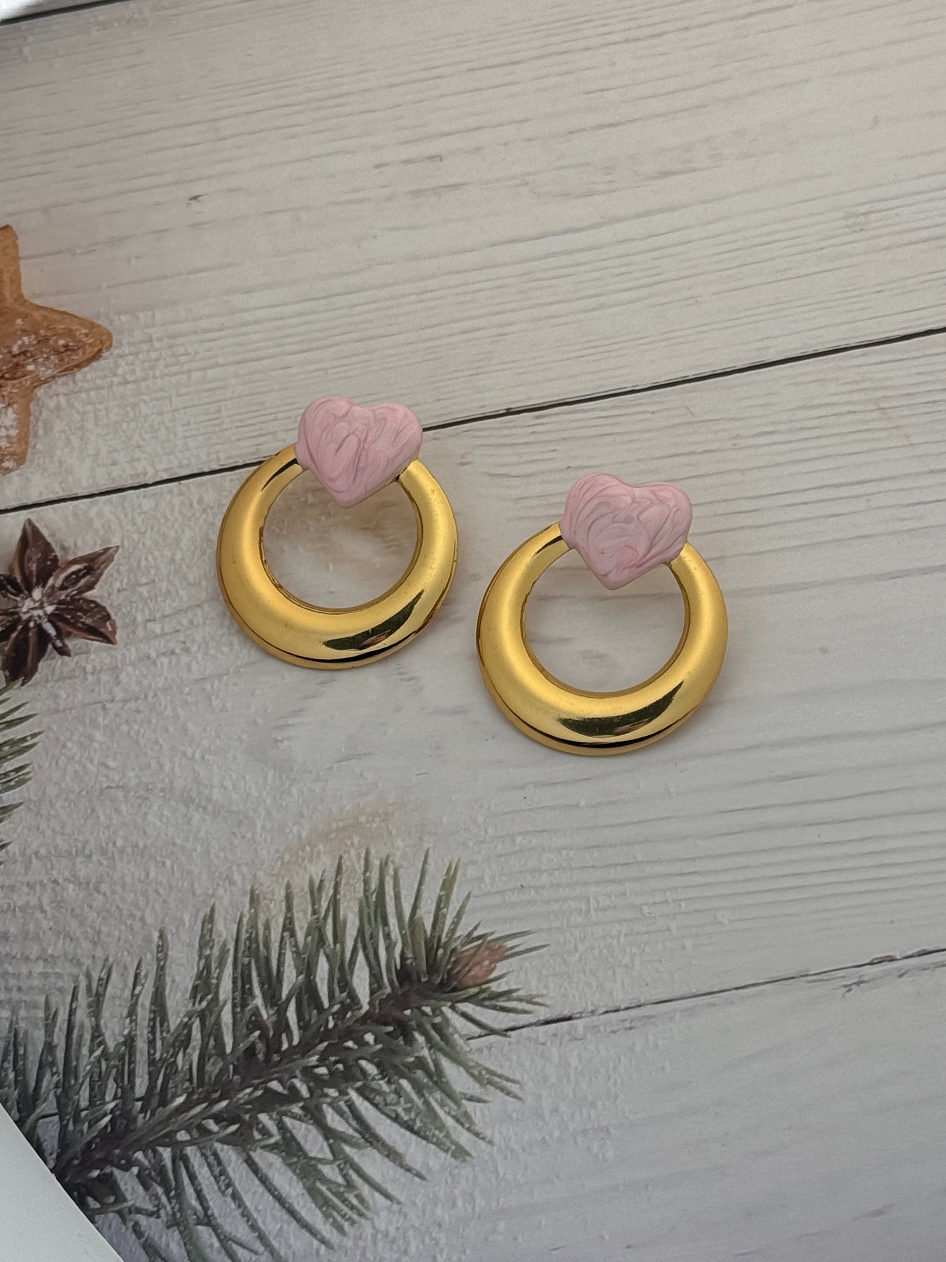 Two gold decorative rings with pink flower-shaped ends on a wooden surface.
