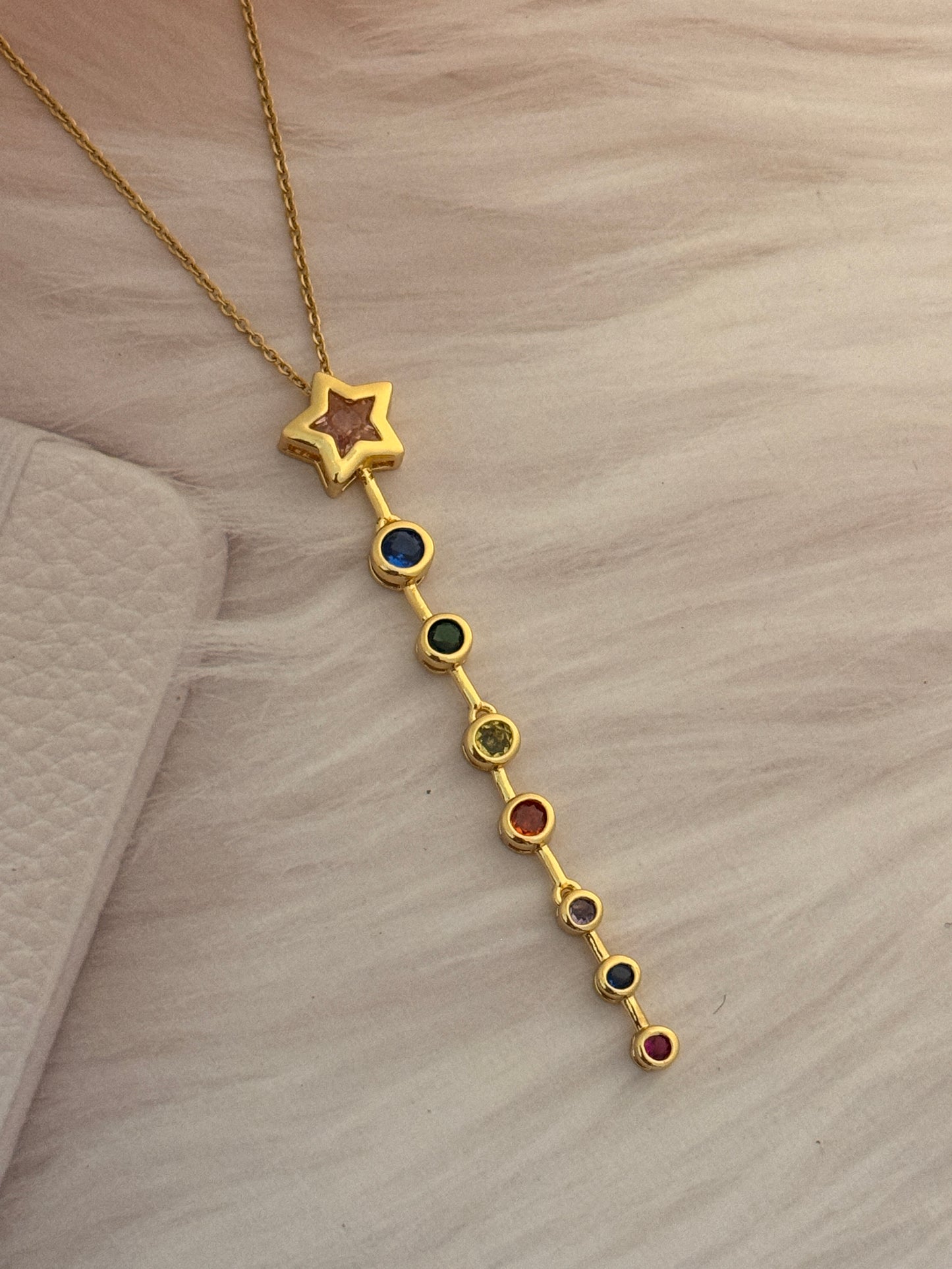 Gold bracelet with star and colorful beads on a light brown surface