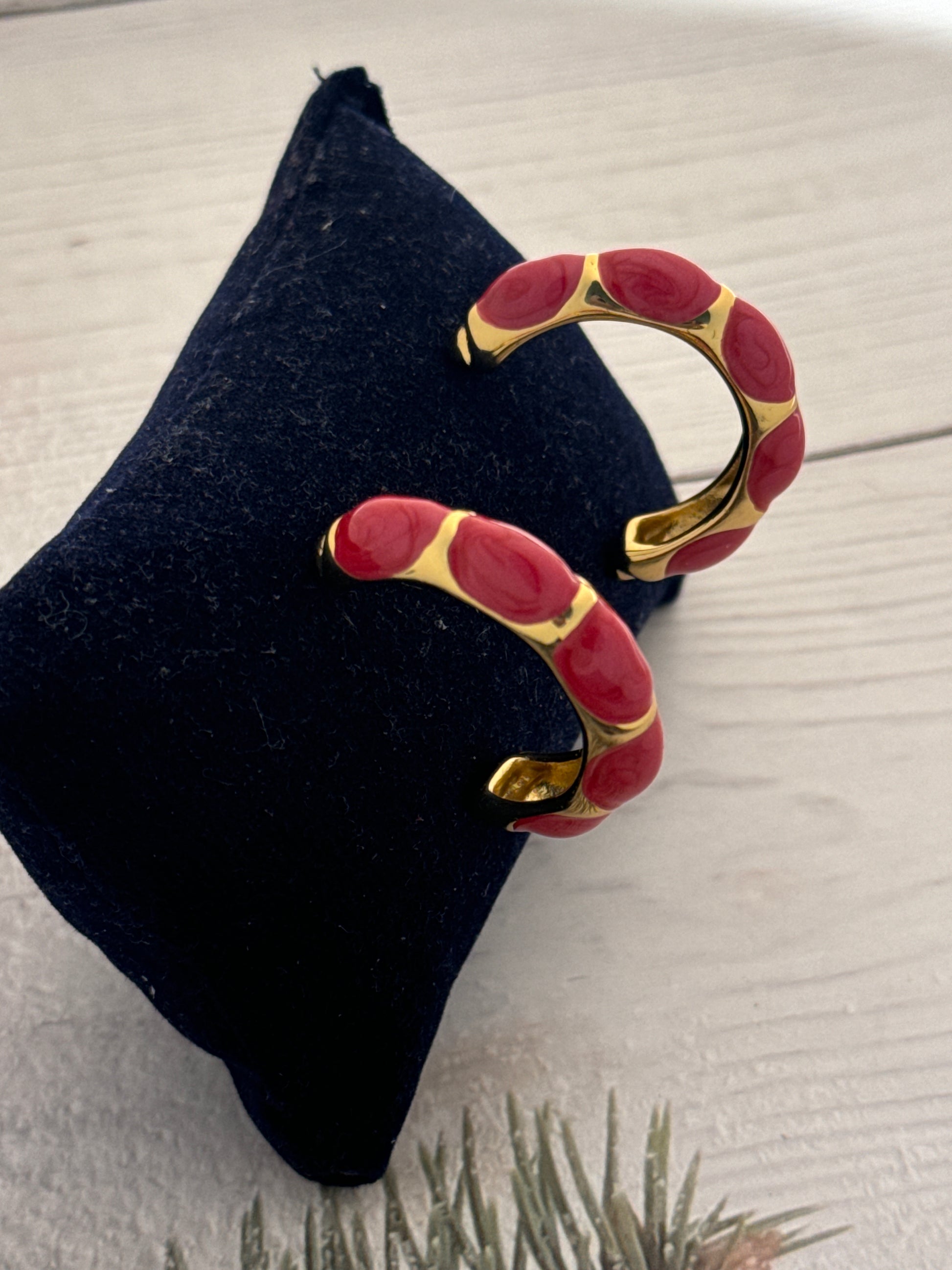 Pair of red and gold earrings on a dark blue stand with a light wooden background