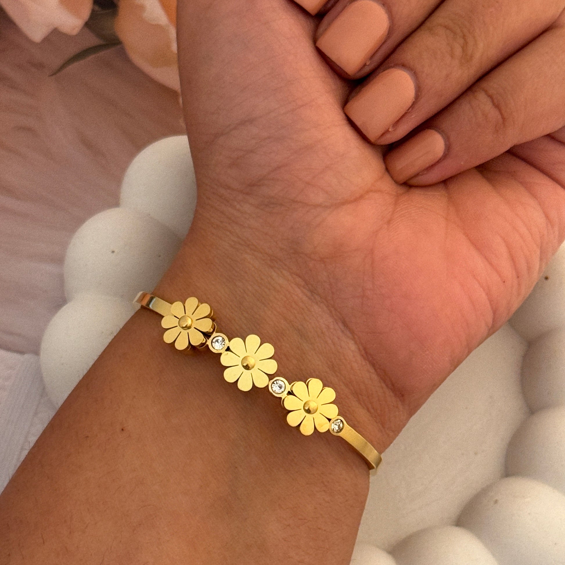 Gold bracelet with floral designs on a wrist against a neutral background