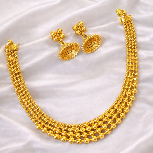 Gold necklace and earrings on a white satin surface