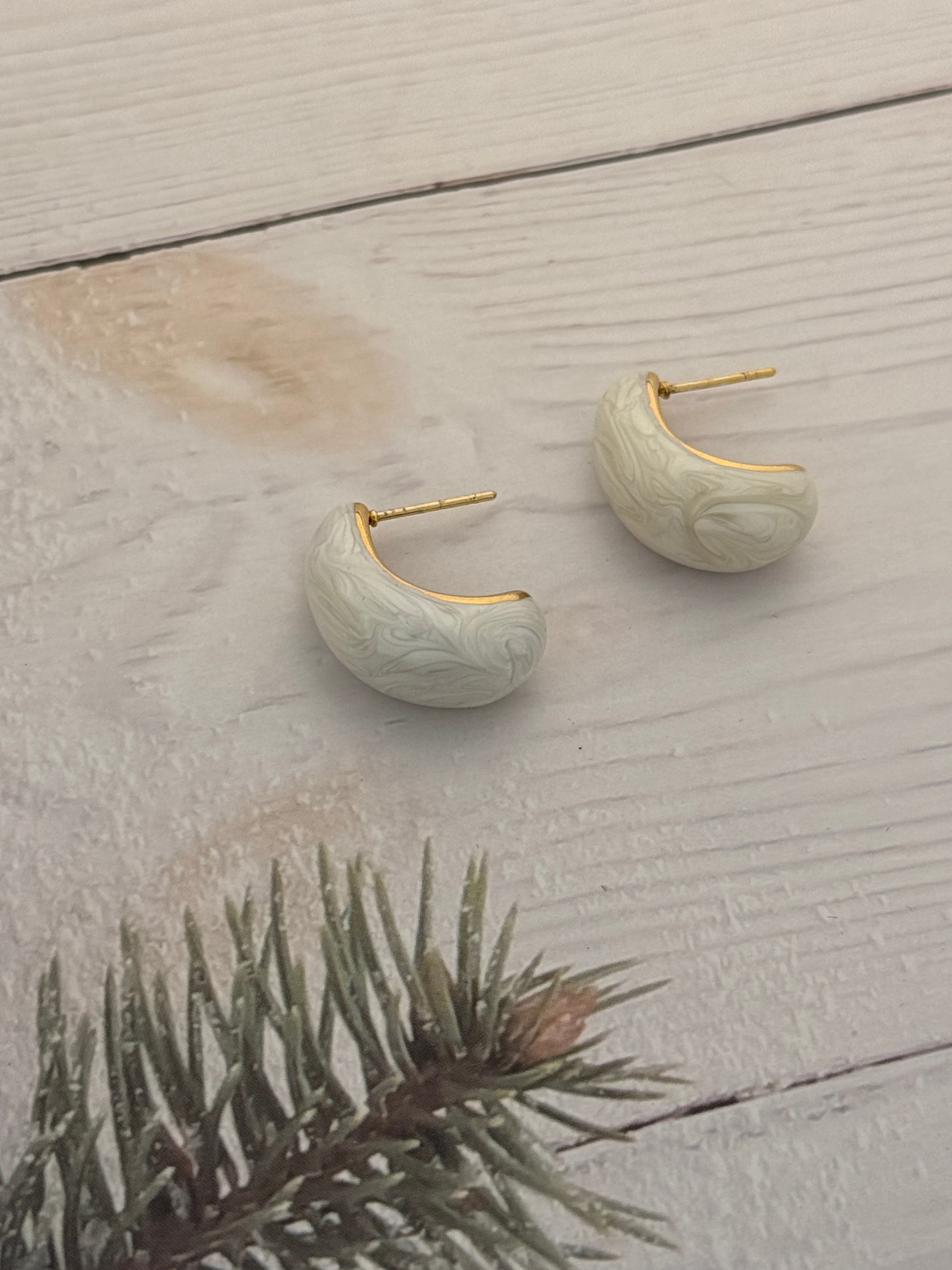 Pair of moon-shaped earrings with gold accents on a light wooden surface.