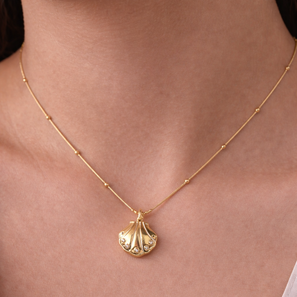 Gold necklace with a pendant on a person wearing a light pink top.