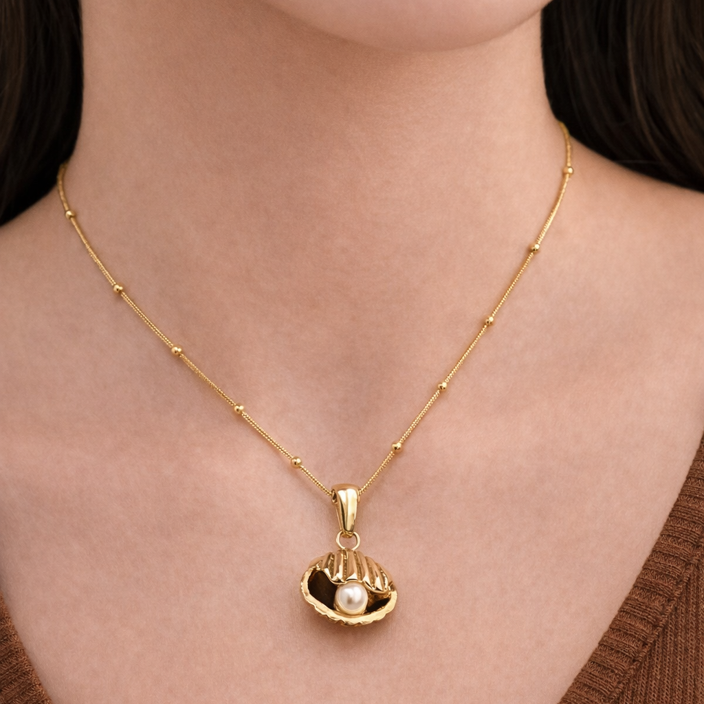 Gold necklace with a pendant featuring a pearl on a person wearing a brown top.