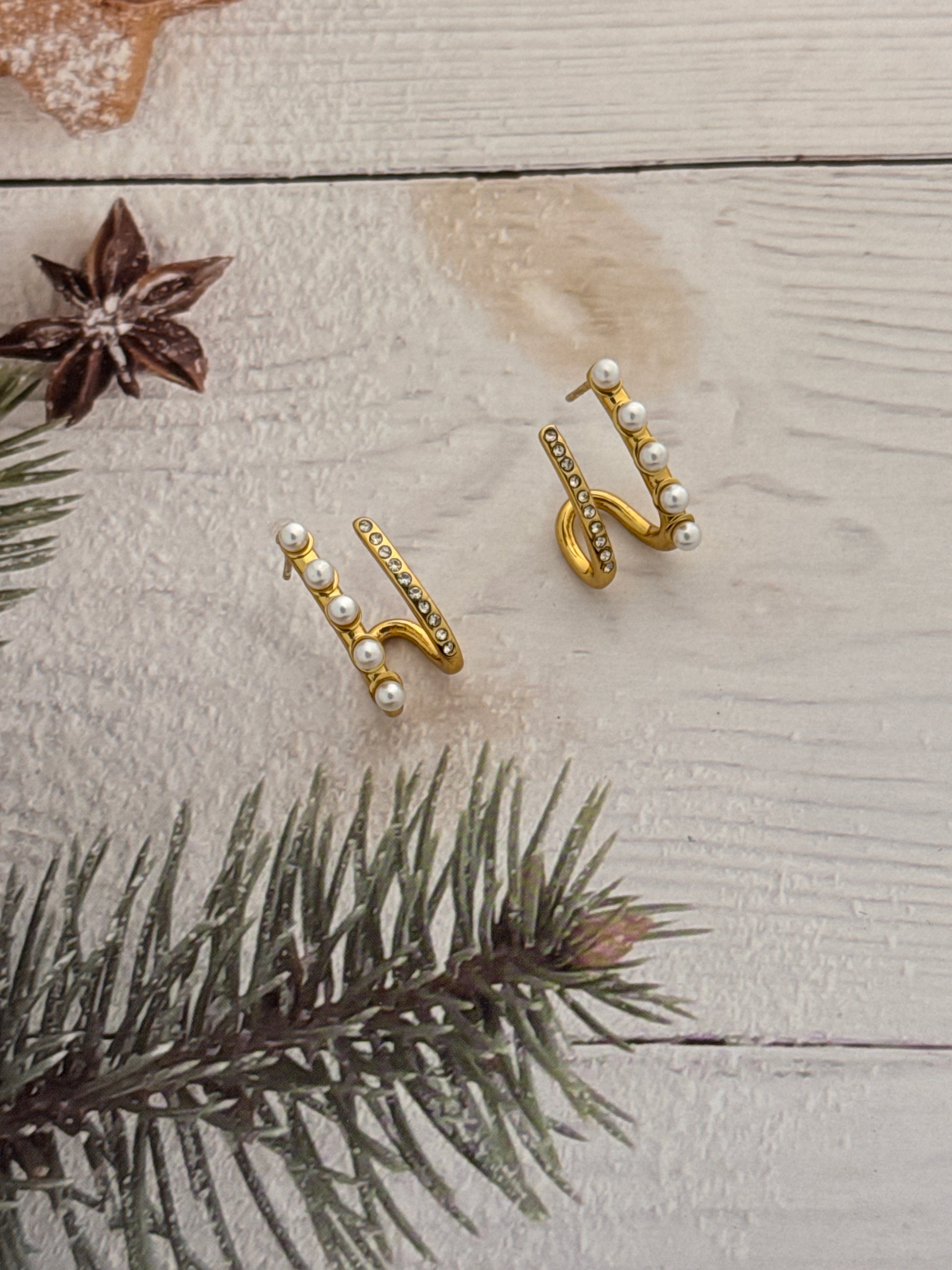 Gold earrings with pearls on a wooden surface with a pine branch and star anise.