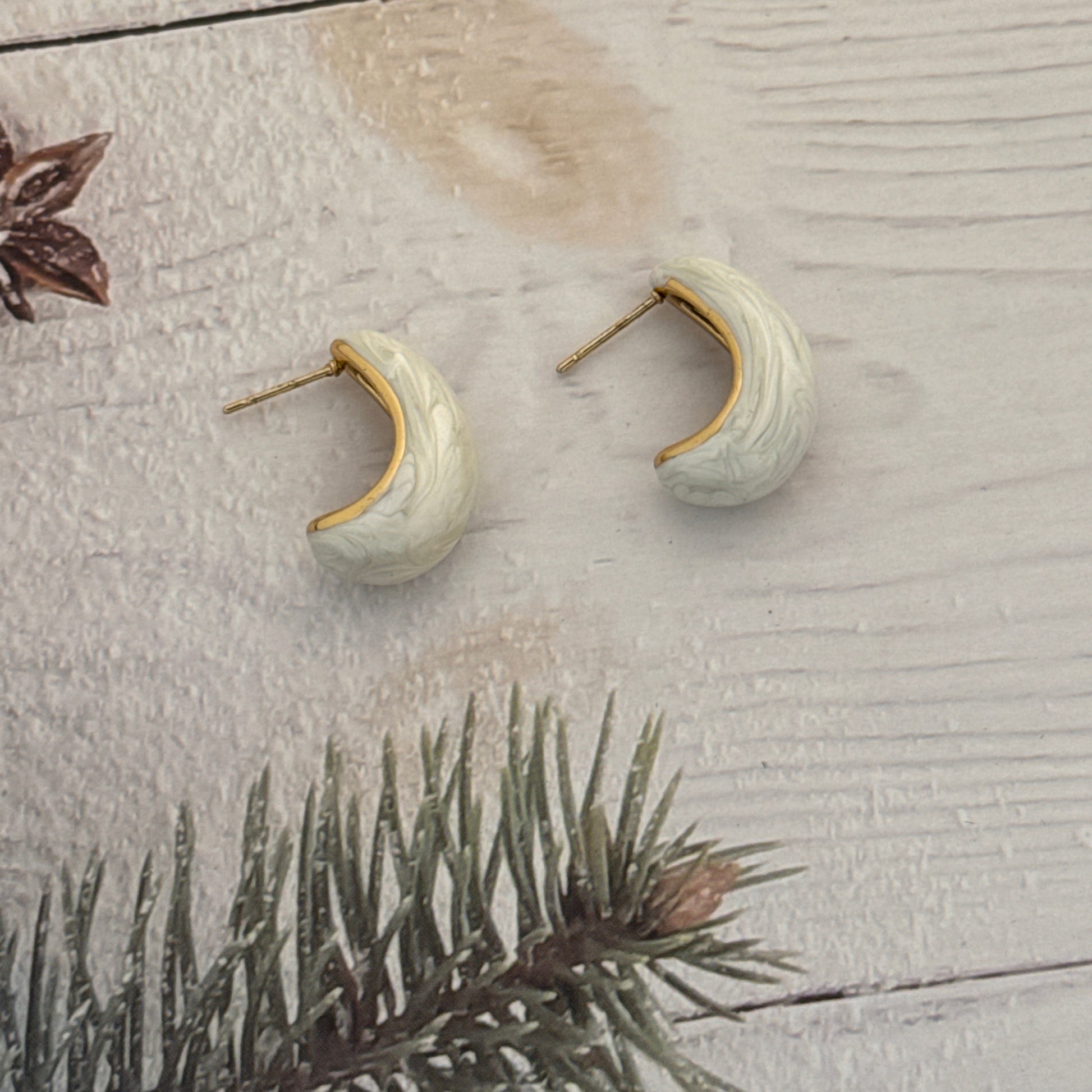 Pair of ceramic earrings on a textured surface with a branch in the background