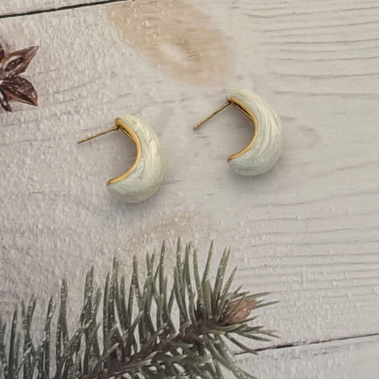 Pair of ceramic earrings on a textured surface with a branch in the background