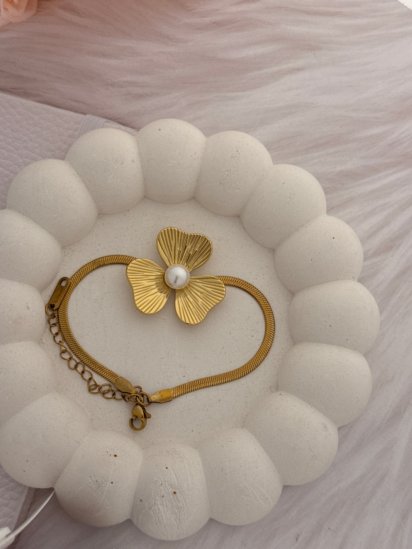Gold bracelet with a floral design and pearl on a textured white surface
