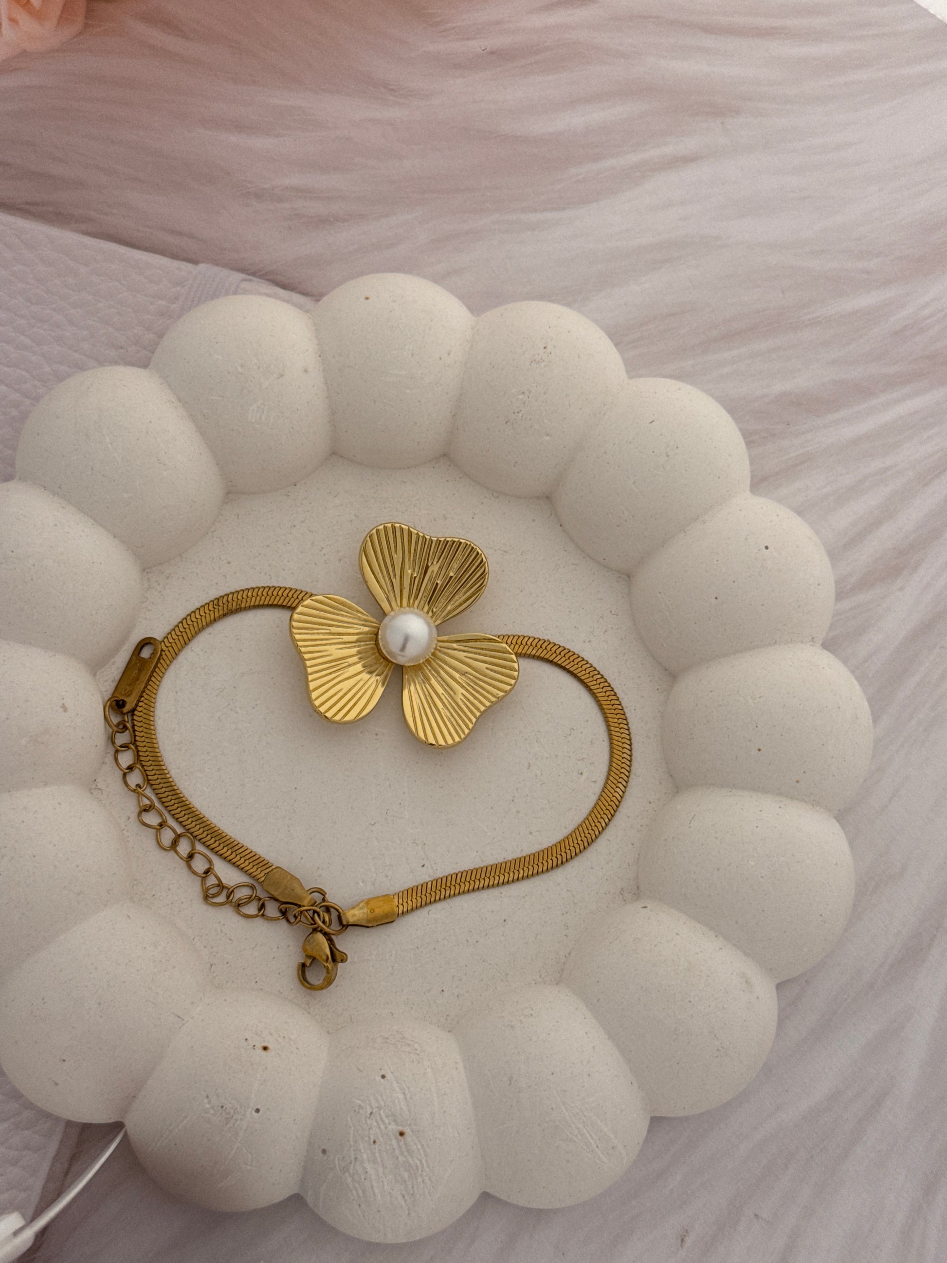 Gold bracelet with a floral design and pearl on a textured white surface