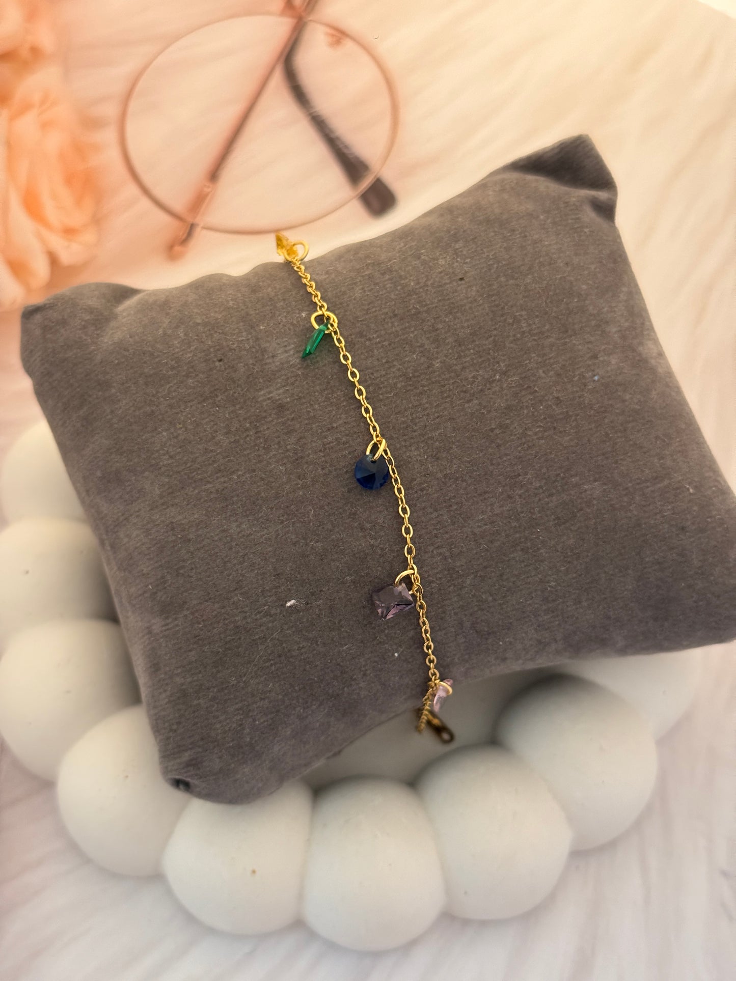 Gold bracelet with colorful stones on a gray cushion