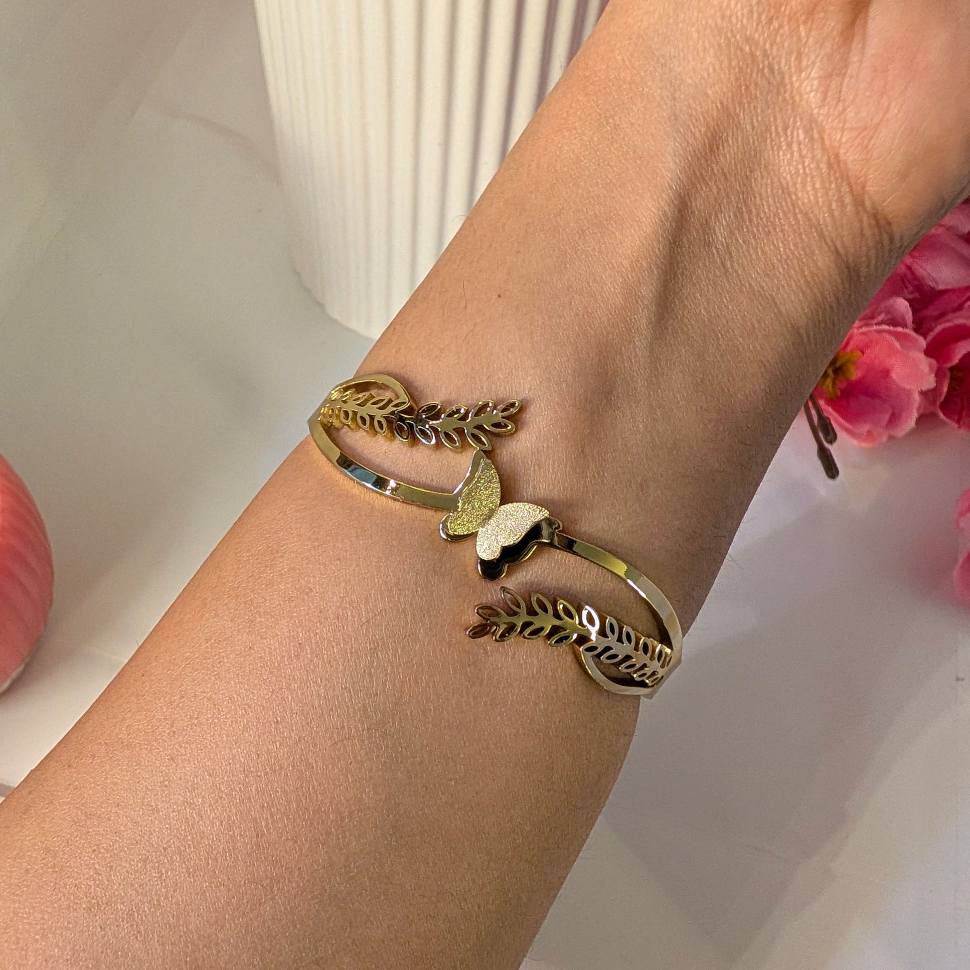 Gold bracelet with leaf design on a wrist against a light background