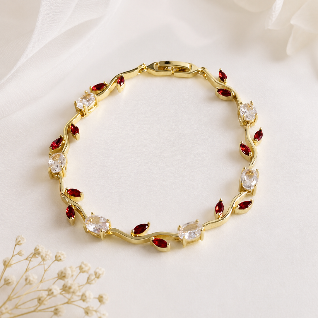 Gold bracelet with red and clear stones on a white fabric background