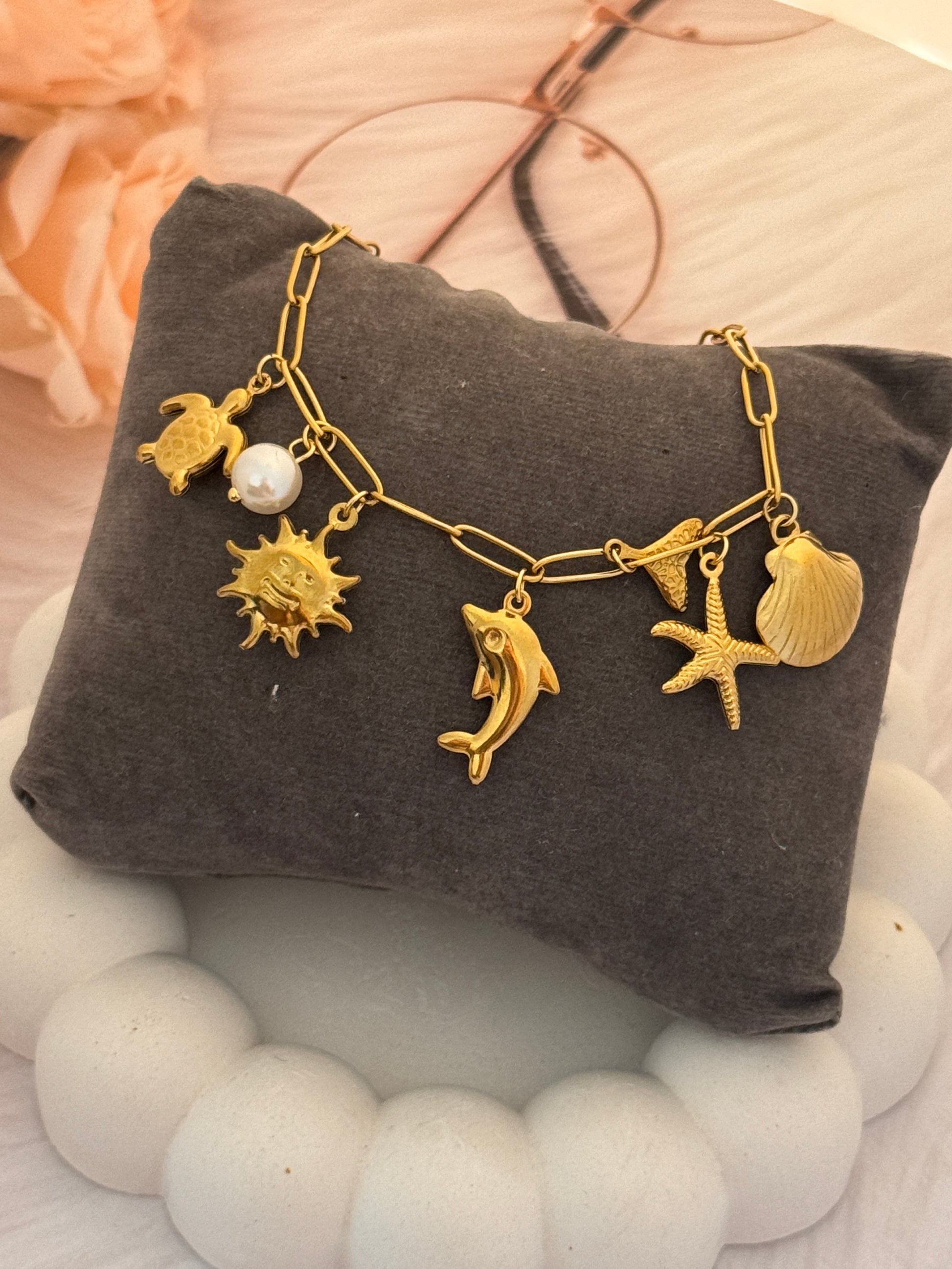 Gold bracelet with sea-themed charms on a gray pillow