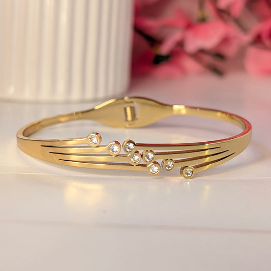 Gold bracelet with small diamonds on a white surface with pink flowers in the background