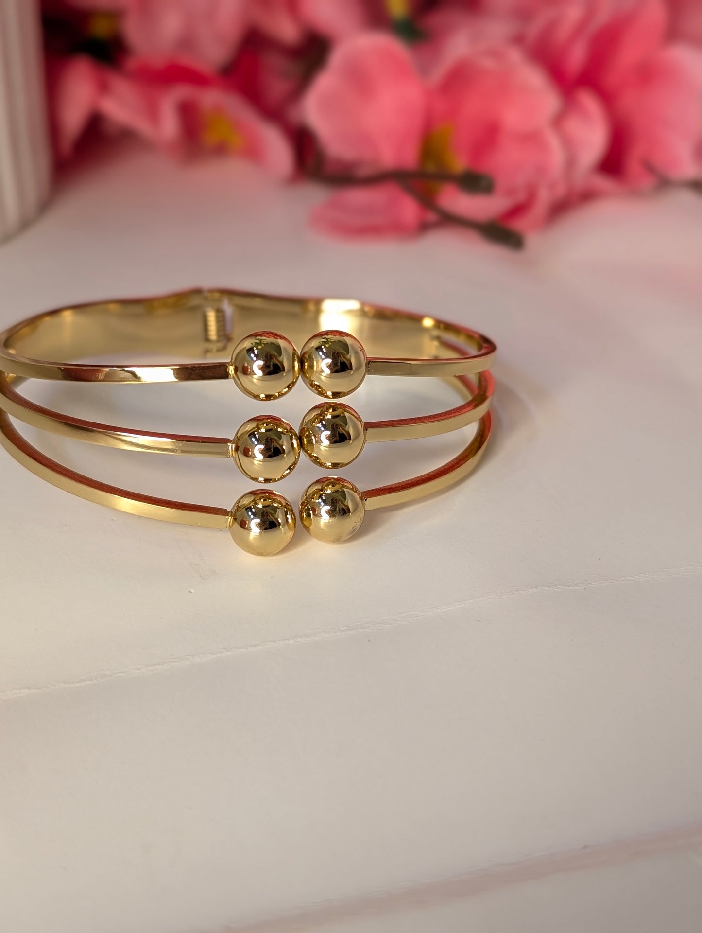 Gold bracelet with spherical embellishments on a white surface with pink flowers in the background