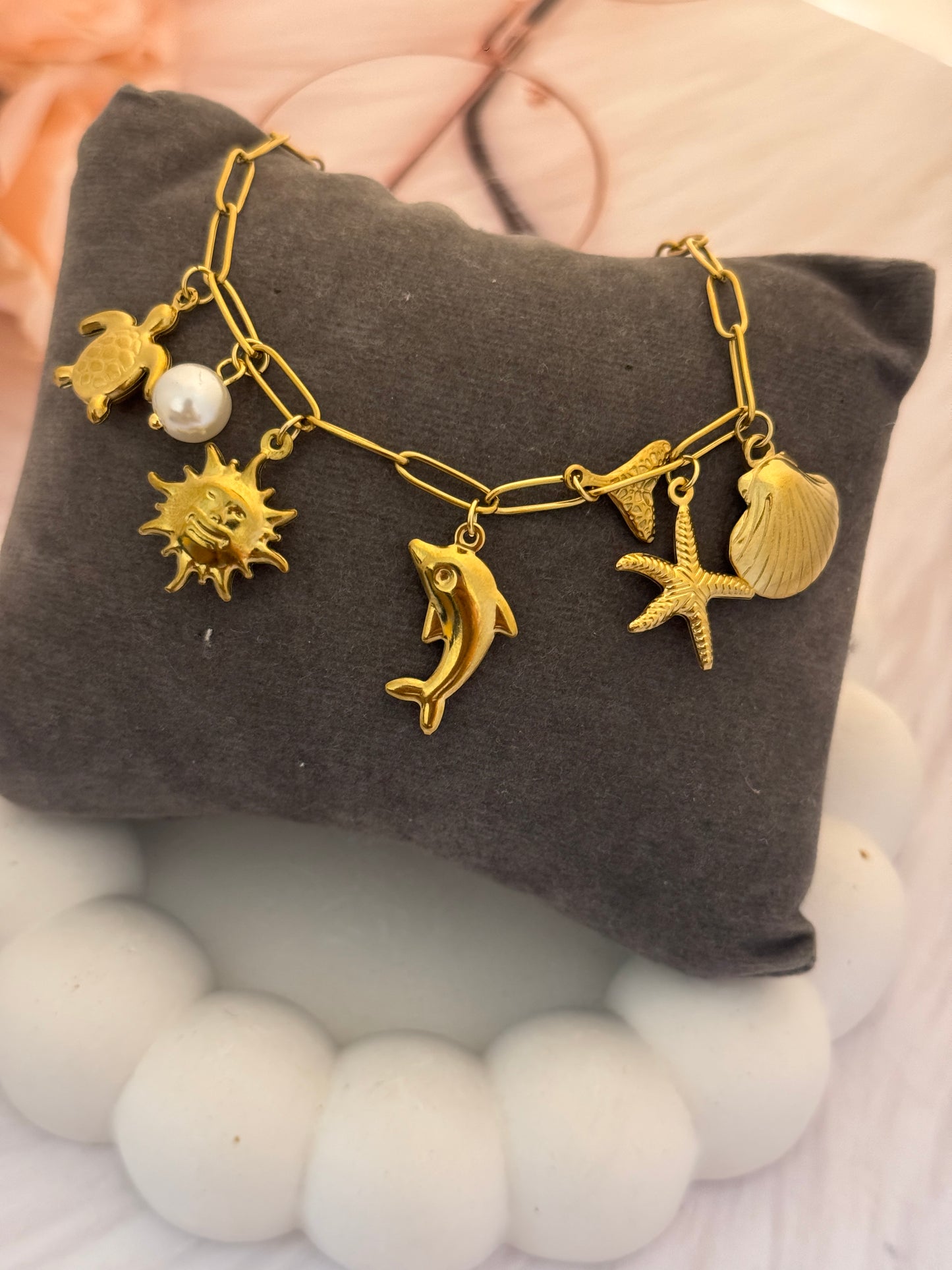Gold bracelet with various charms on a gray pillow