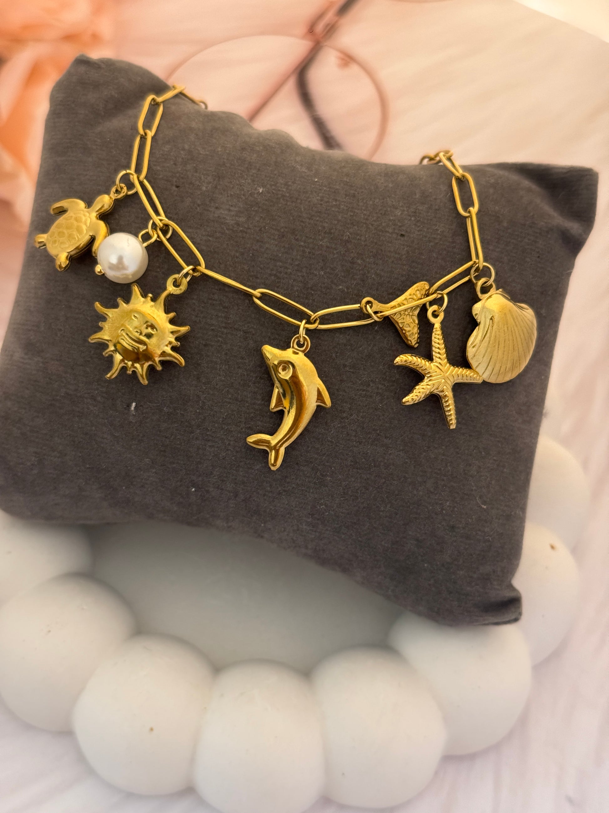 Gold bracelet with various charms on a gray pillow