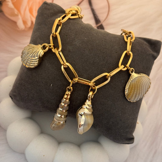 Gold chain bracelet with shell charms on a gray pillow