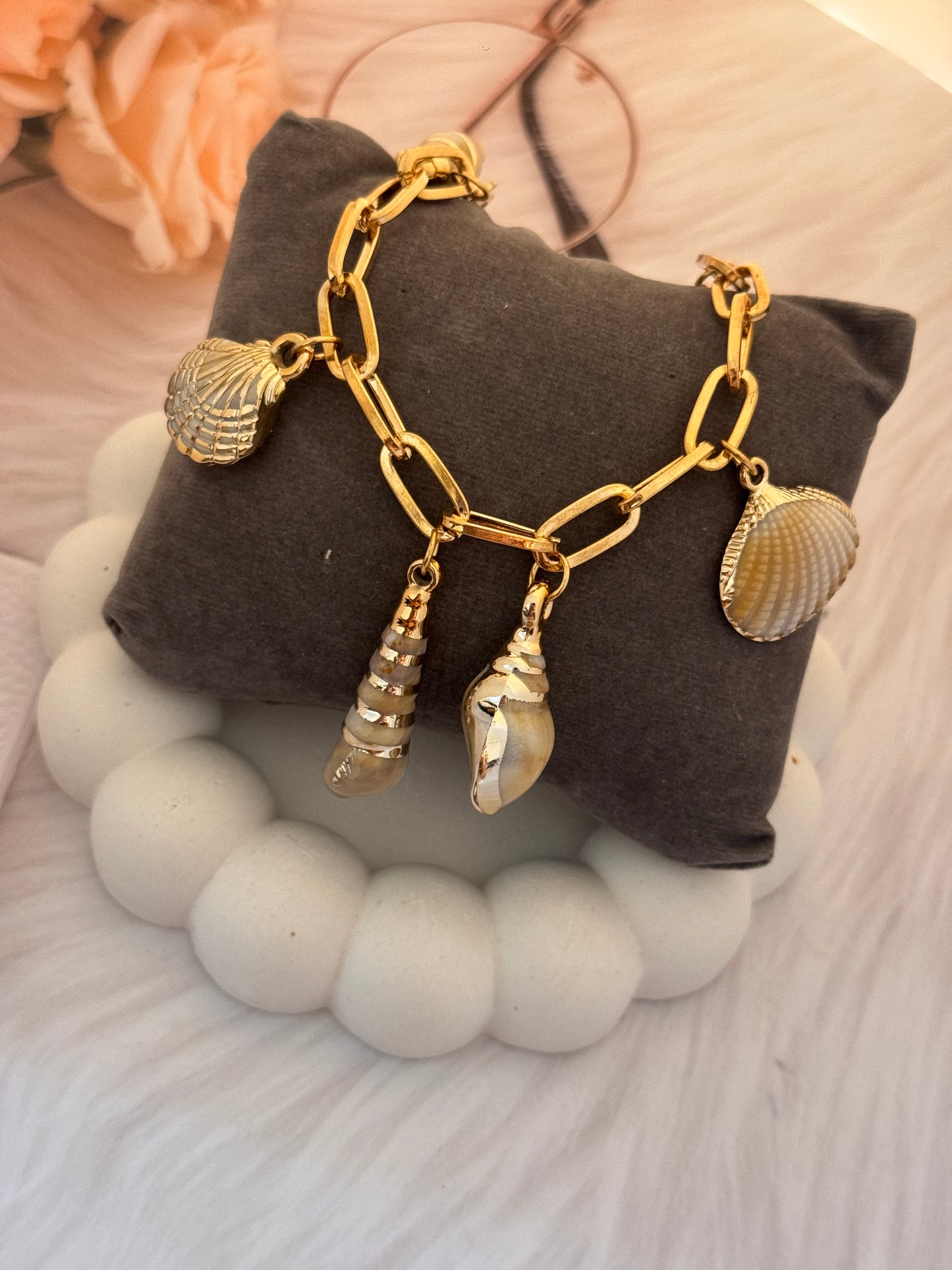 Gold chain bracelet with shell charms on a gray pillow