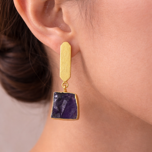 Gold earring with a purple stone worn by a person
