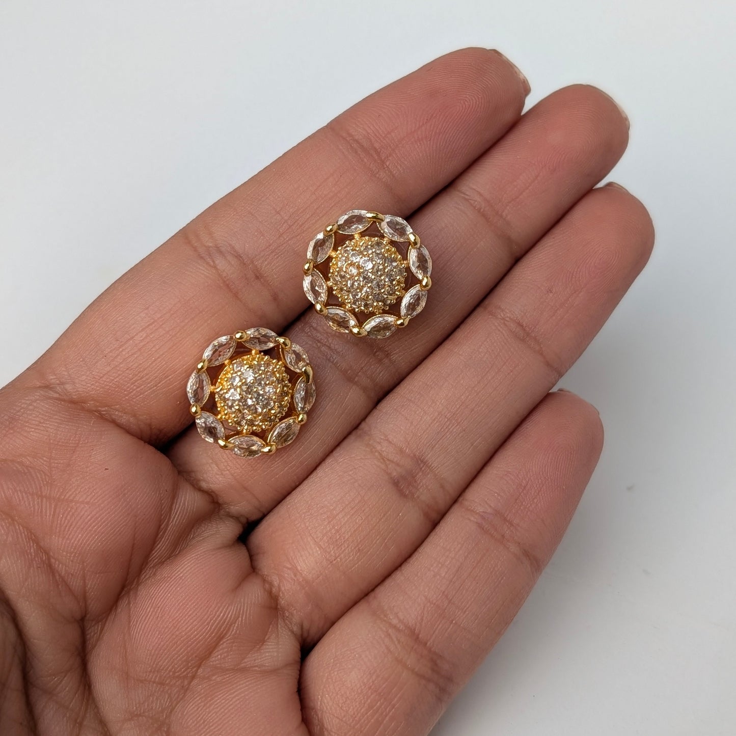 Gold earrings with gemstones held between fingers on a white background