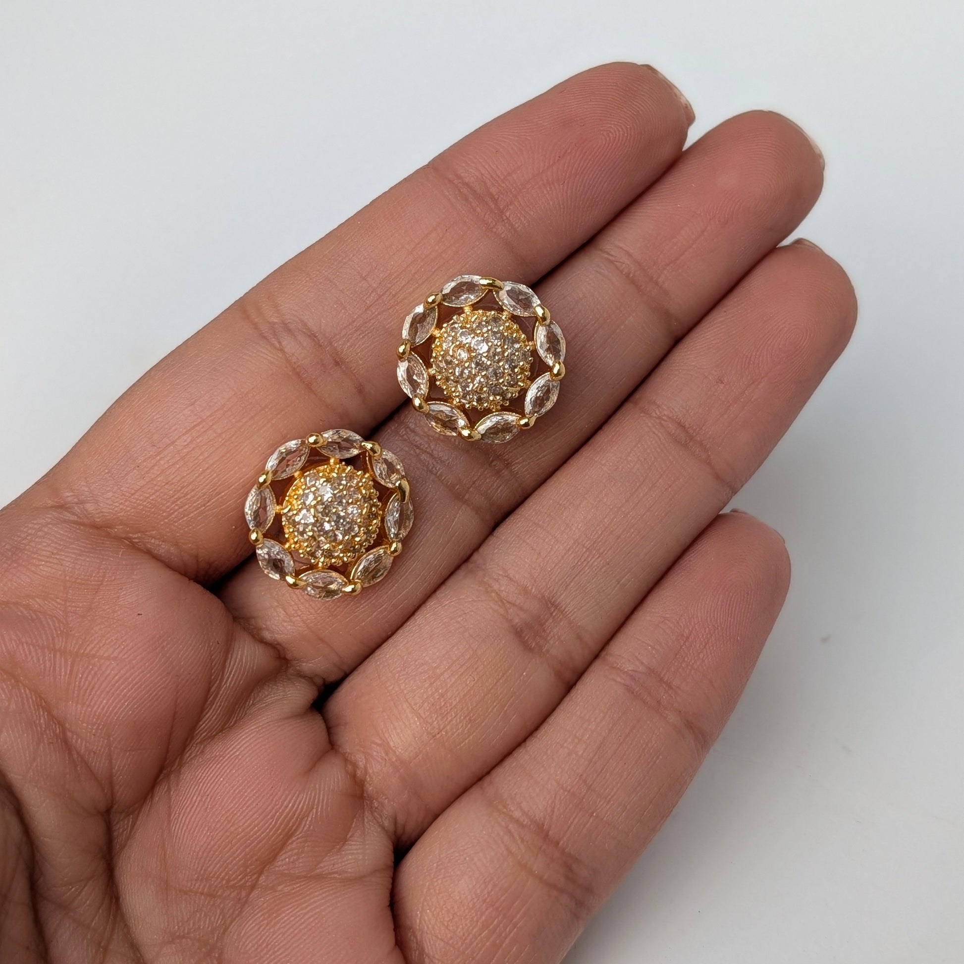 Gold earrings with gemstones held between fingers on a white background