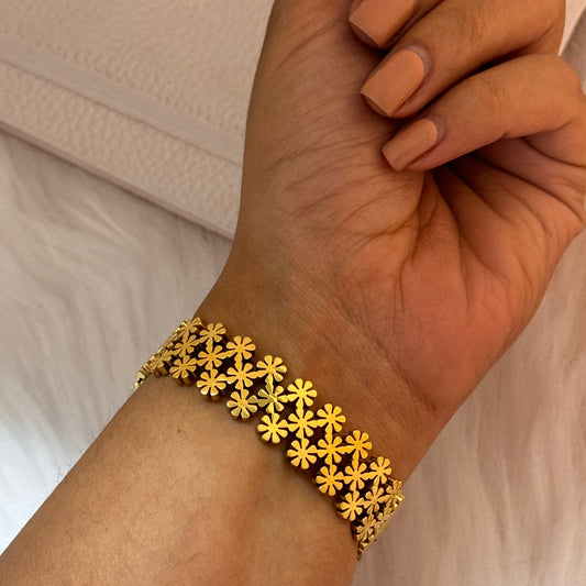 Gold floral bracelet on a wrist with a neutral background