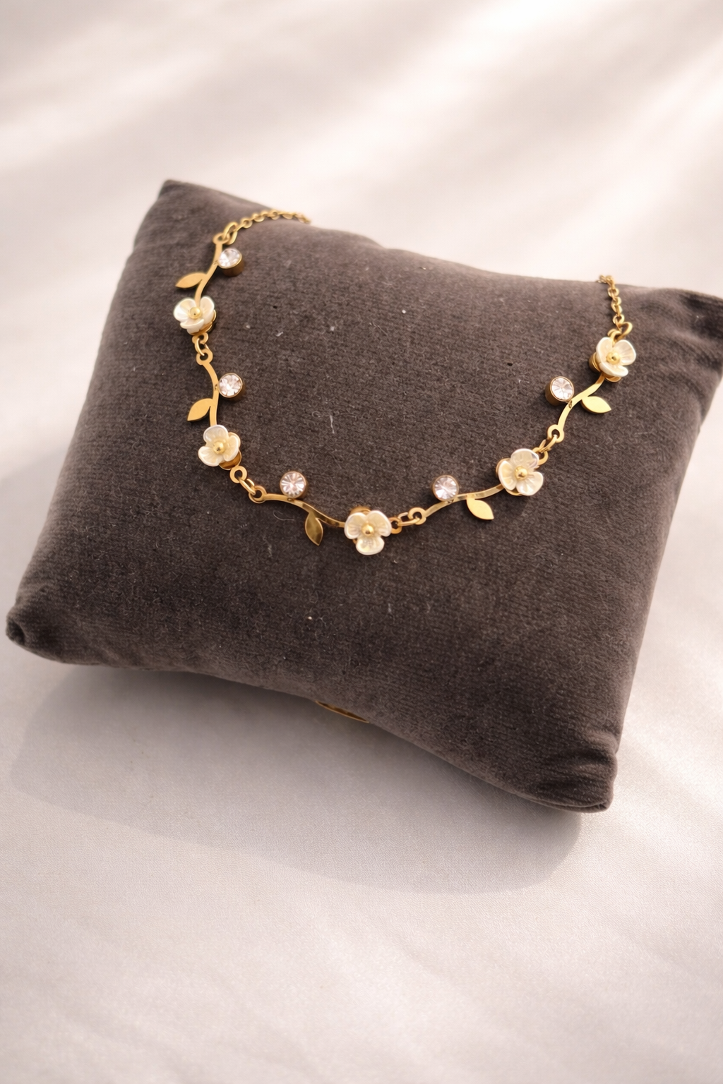 Gold floral necklace on a gray cushion with a white background