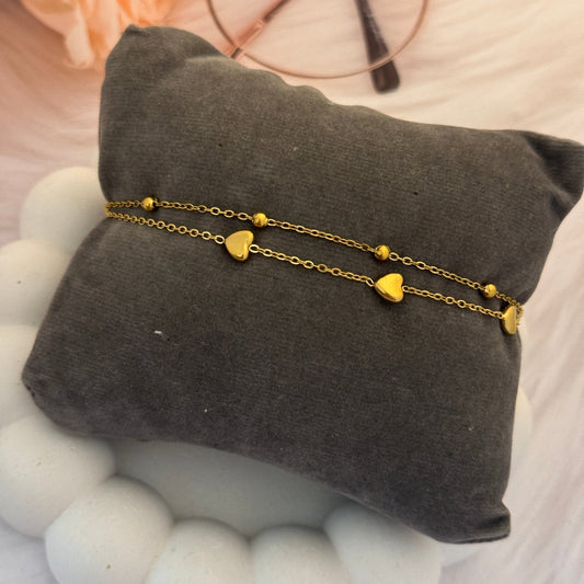Gold heart-shaped bracelet on a gray cushion with a blurred background