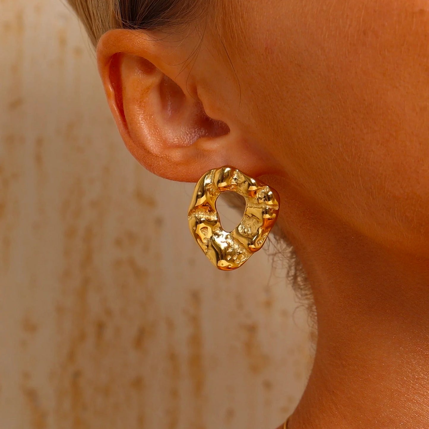 Gold hoop earring worn by a person with a neutral background