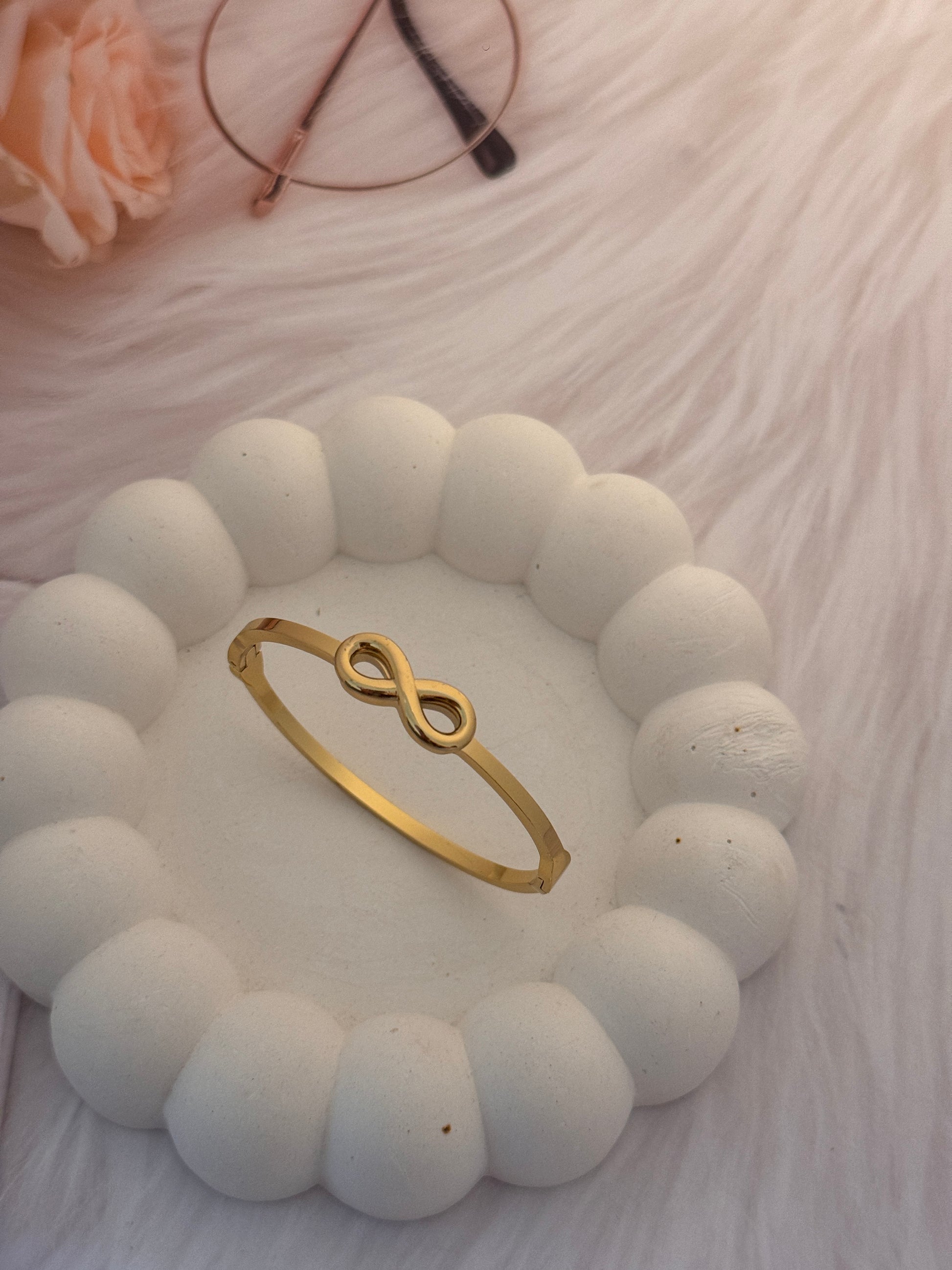 Gold infinity ring on a white stone surface with a blurred background